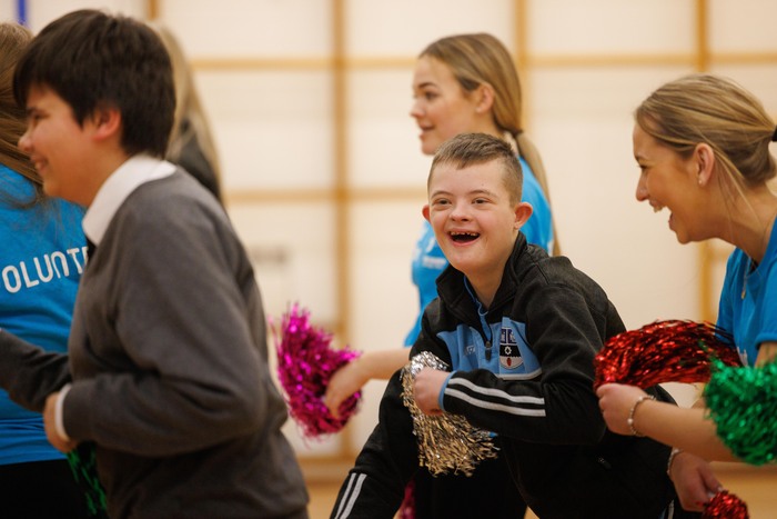 Group of disabled and non-disabled people taking part in a dance session with pom poms in a sports hall.